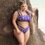 A plus size model wears a purple bandeau-style bra and panty set with a galaxy-inspired planet pattern.