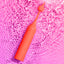 A red Romp Pop cylindrical wand-shaped vibrator sends rippling vibrations through water over a pink background.