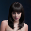 A model wearing a black wig with layers that come just below the collarbones, and has a full fringe.
