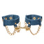 A pair of denim handcuffs with gold chain details sits against a white backdrop. 