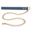 A denim leash lays against a white backdrop attached to a gold chain.