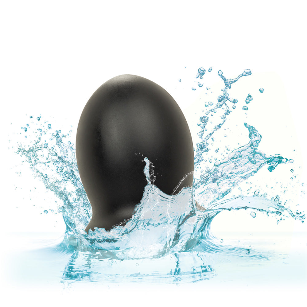 A mini black silicone textured stroker is shown dropped in water showcasing its waterproof design. 