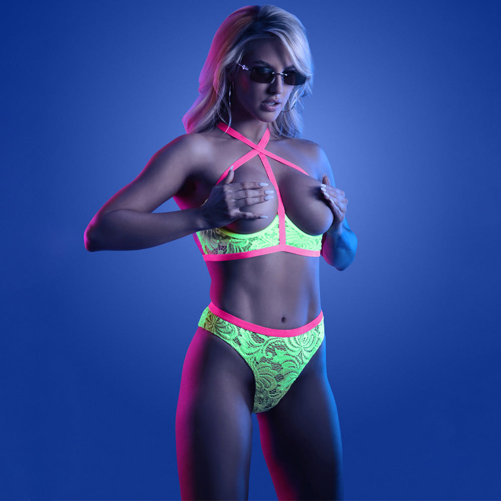 A lingerie model wears a glow-in-the-dark floral lace cupless bra and panty set with a cage strap halter neck design.