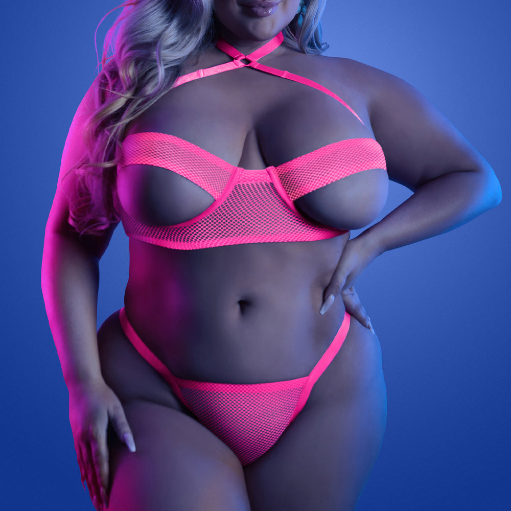A plus size model wears a glow in the dark pink net bra and panty set with peekaboo underboob cutouts.