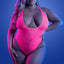 A plus-size lingerie model wears a glow-in-the-dark neon pink teddy with a plunging scoop neck and high-cut legs.