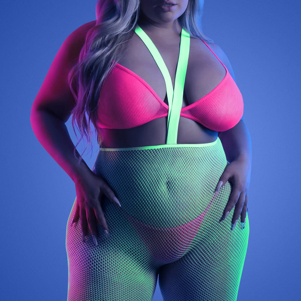 A plus size model wears a glow in the dark fishnet suspender stocking set in neon green and with a pink bralette and panty.