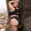 Back view of a plus size model wearing a black crop bra and panty with bikini cut bottoms.