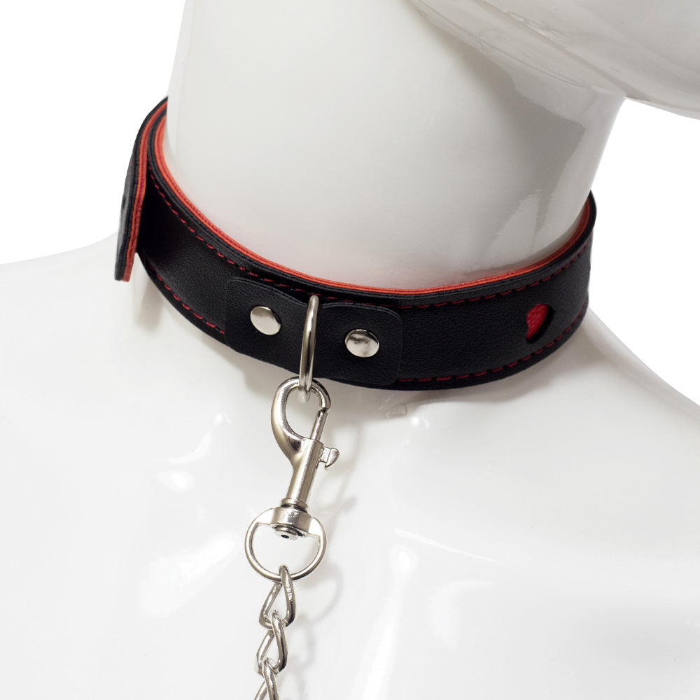 A black faux leather collar with a silver chain leash attached to the collars D-ring is worn around a mannequin's neck.