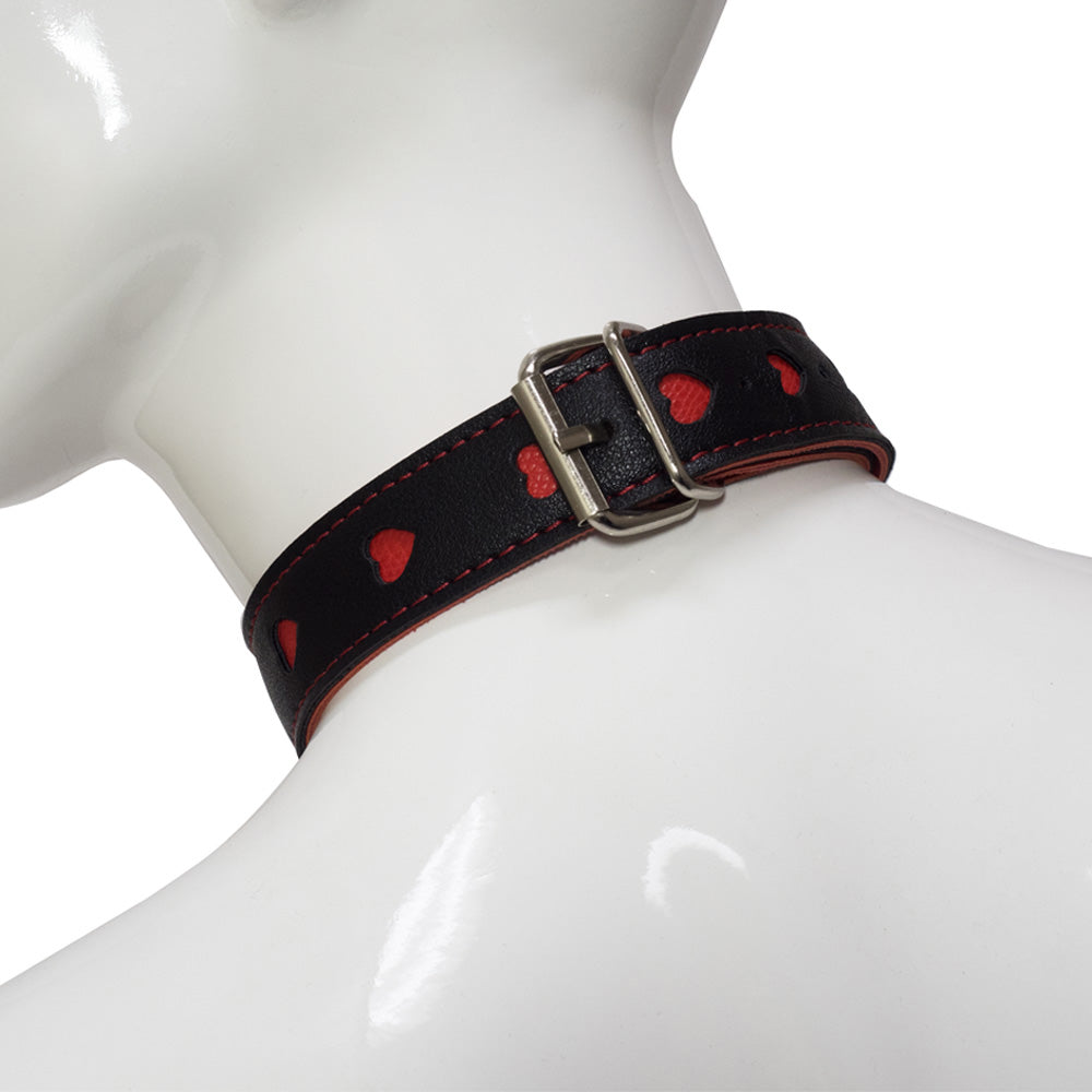 Back view of a faux black leather collar with cutout red hearts, showcasing its adjustable silver buckle and tail keeper.