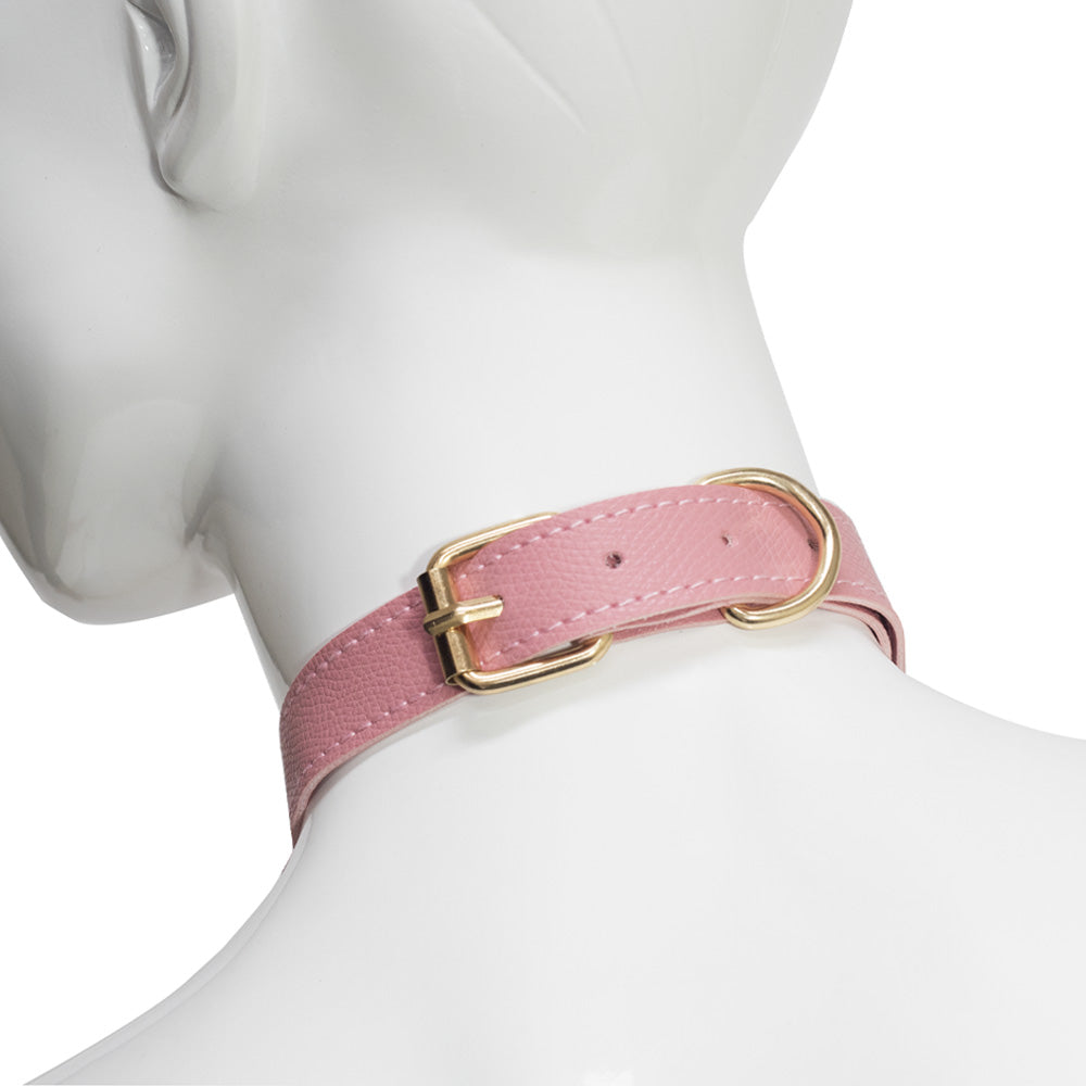 A back view of a pink faux leather collar showcases an adjustable gold buckle and tail keeper around a mannequin's neck.
