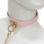 A mannequin wears a baby pink leather collar with a gold T-plate and O-ring attached to a gold chain leash.