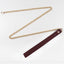 A gold metal chain leash with snap hook closure and a burgundy red leather wrist loop lies flat on a white background.