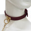 A mannequin wears a burgundy red leather collar with a gold T-plate and O-ring attached to a gold chain leash.