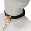 A mannequin wears a black leather collar with a gold T-plate and O-ring attached to a gold chain leash.