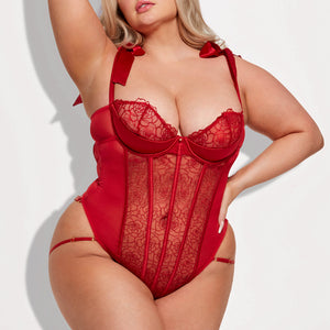 A curvy model wears a sheer red rose-patterned teddy with frilly petal edges above the cups and satin-tie shoulder straps.