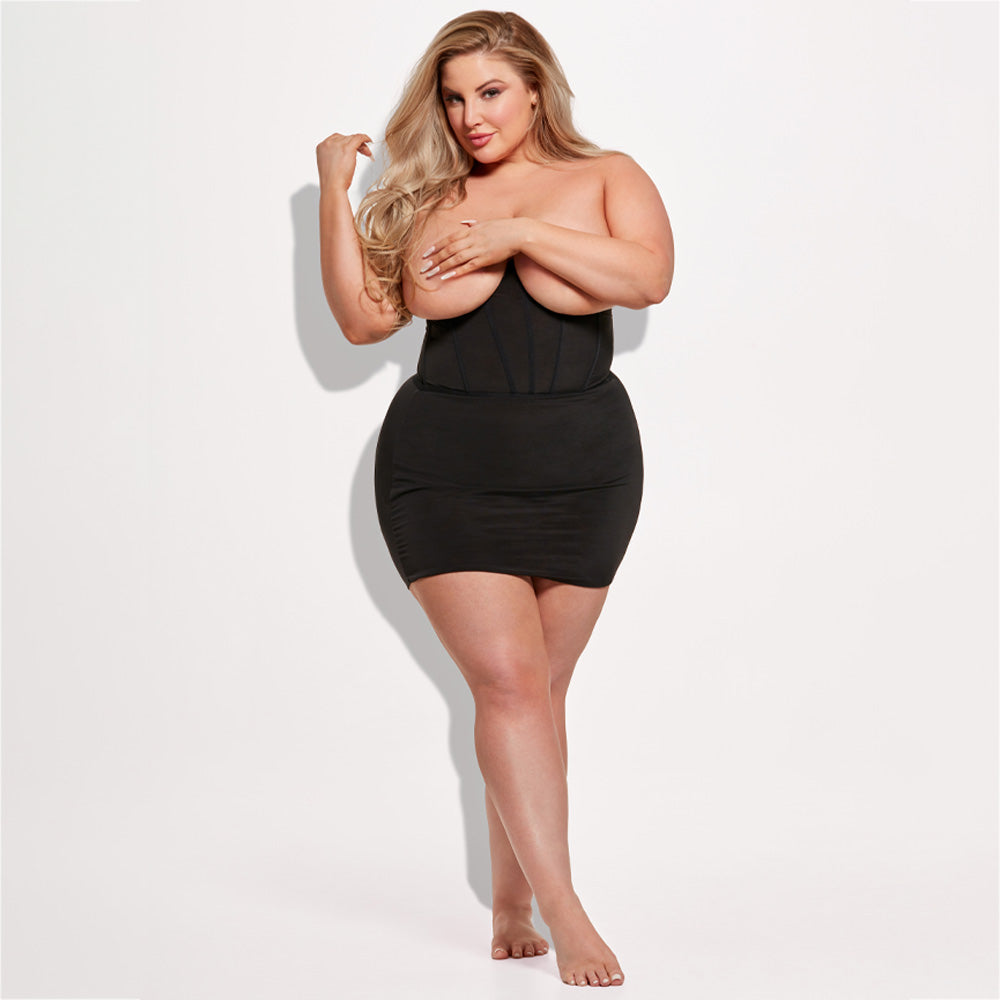 A plus-size lingerie model wears a cupless shapewear slip in black with a boned underbust bodice design.