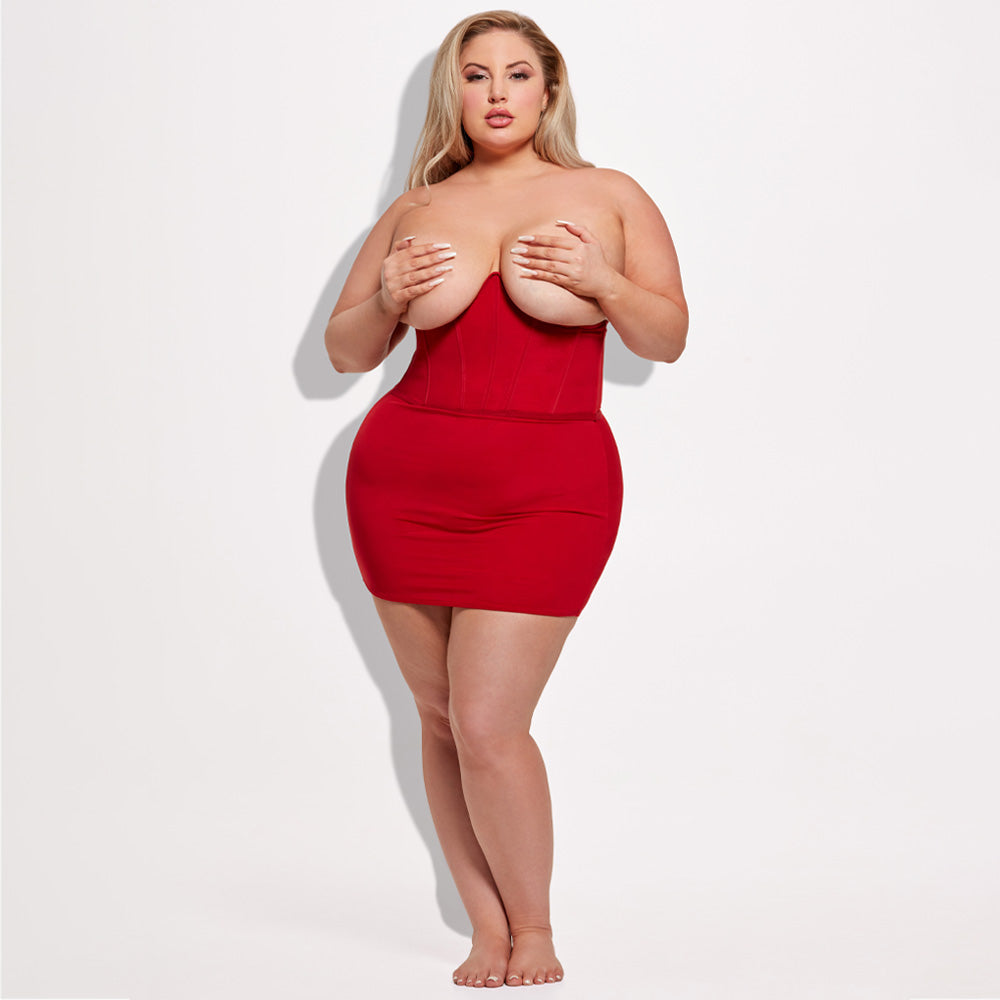 A plus-size lingerie model wears a cupless shapewear slip in red with a boned underbust bodice design.