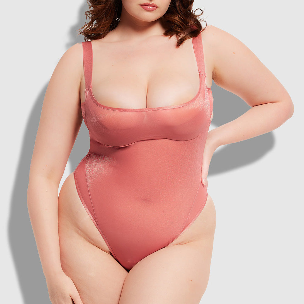 A curvy lingerie model wears a light pink sheer mesh layered bra bodysuit with a scoop neck and underwired demi-cups.