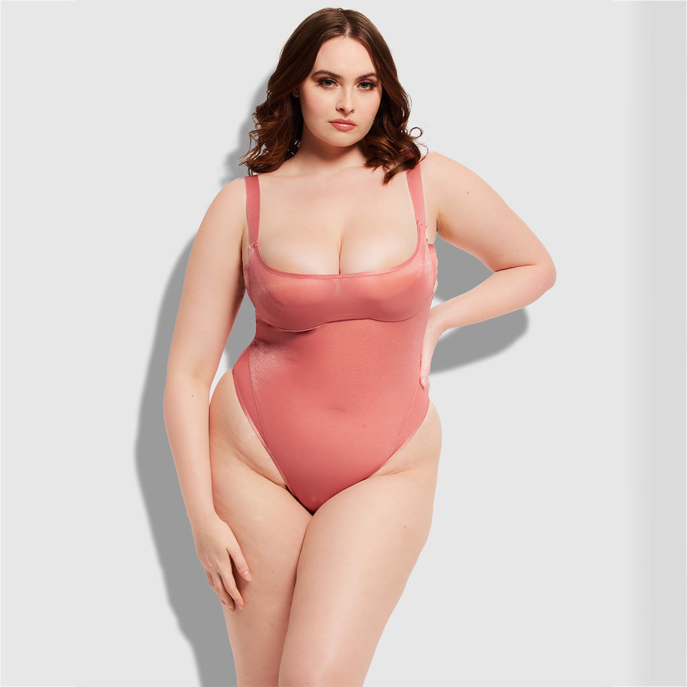 A curvy lingerie model wears a light pink sheer mesh bra bodysuit featuring thick, adjustable elastic shoulder straps.