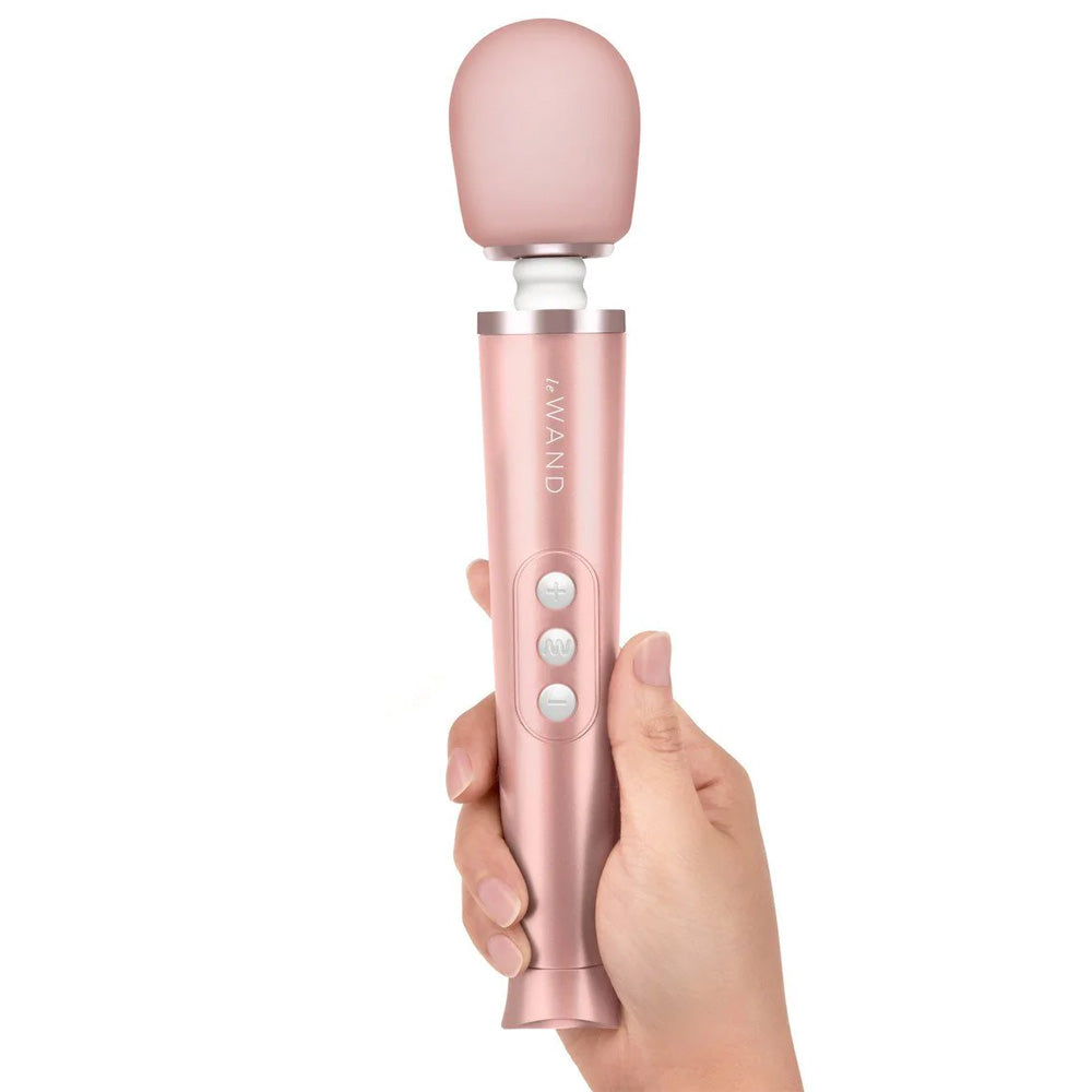 A hand model holds a Le Wand petite rose gold vibrator and shows its three control buttons. 