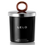 A Lelo vanilla and creme de cacao candle sits against a white backdrop featuring a O shaped handle on the top of the lid. 