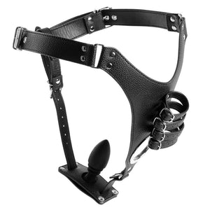 A faux leather male chastity harness with a silicone anal plug and buckled penis straps sits on a white background.