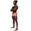 A model poses in front of a white backdrop wearing orange cutout boxer briefs with a sheer geometric stripe pattern.