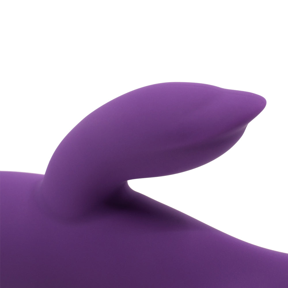 A close up of a dark purple silicone rabbit vibrator's clitoral stimulator against a white background.