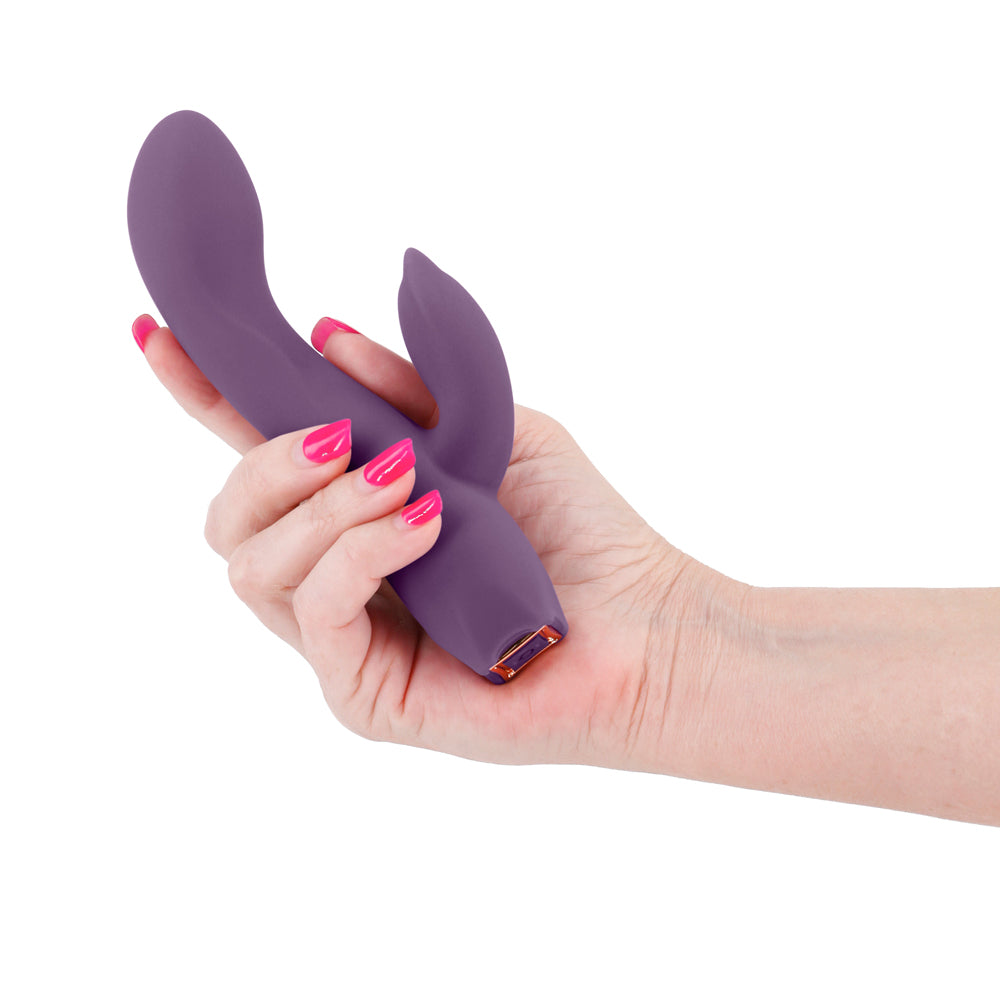 A manicured hand holds a dark purple silicone G spot rabbit vibrator for scale.
