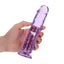 A hand model holds a purple crystal clear jelly dildo that features a harness-compatible suction cup base. 