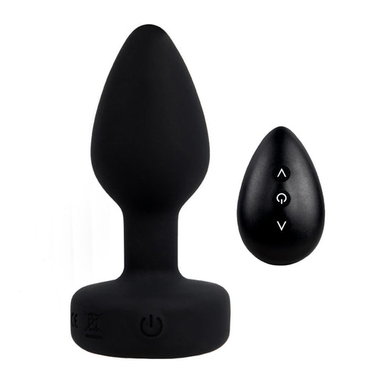 A petite black remote control vibrating gem butt plug stands on a white backdrop next to its mini remote control with three buttons on it.