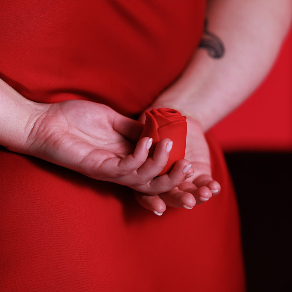 A close up of a model holding a Rose Ravish clitoral suction stimulator in red behind her back.