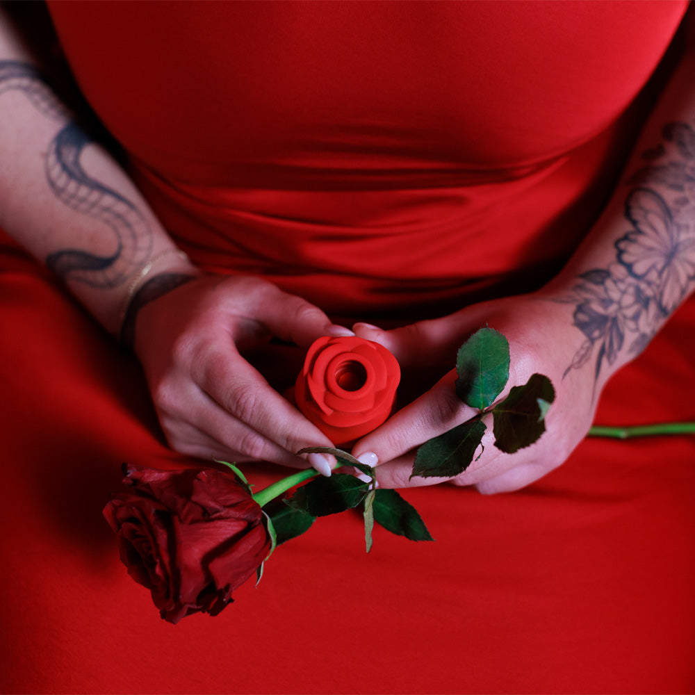 A model holds a Rose Ravish clitoral stimulator shaped like a rose in her lap with a red rose.