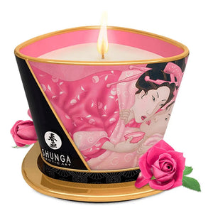 Shunga Aphrodisia rose petals scented massage candle sits with its flame burning and roses around it. 