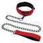 A red heart charm collar and chain leash lays flat against a white backdrop. 