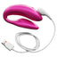 A pink silicone couples vibrator sits against a white backdrop with its magnetic USB charging cord attached.