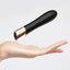 A hand for scale underneath a mini black bullet vibrator with gold ring base.