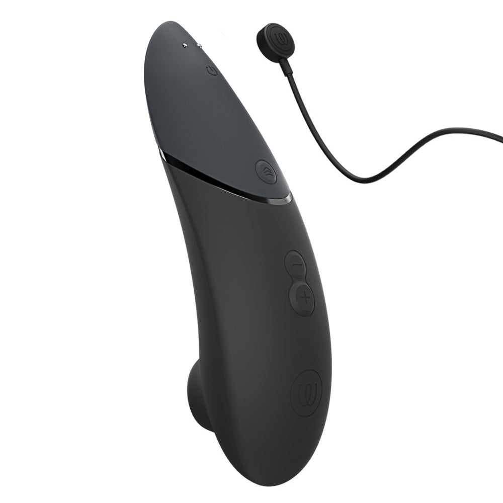 A black silicone clitoral stimulator stands next to its magnetic charging cord.