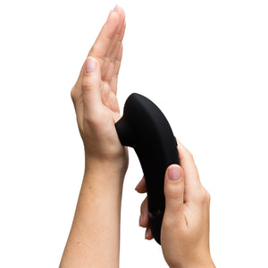 A hand model holds a clitoral stimulator with the suction chamber pressed against their palm.