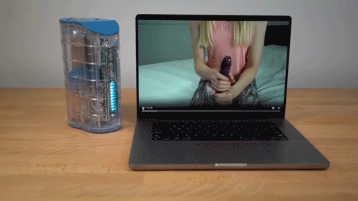 A laptop shows a pornstar stroking a dildo while the Autoblow Ultra next to it mimics her stroking motions in real-time.