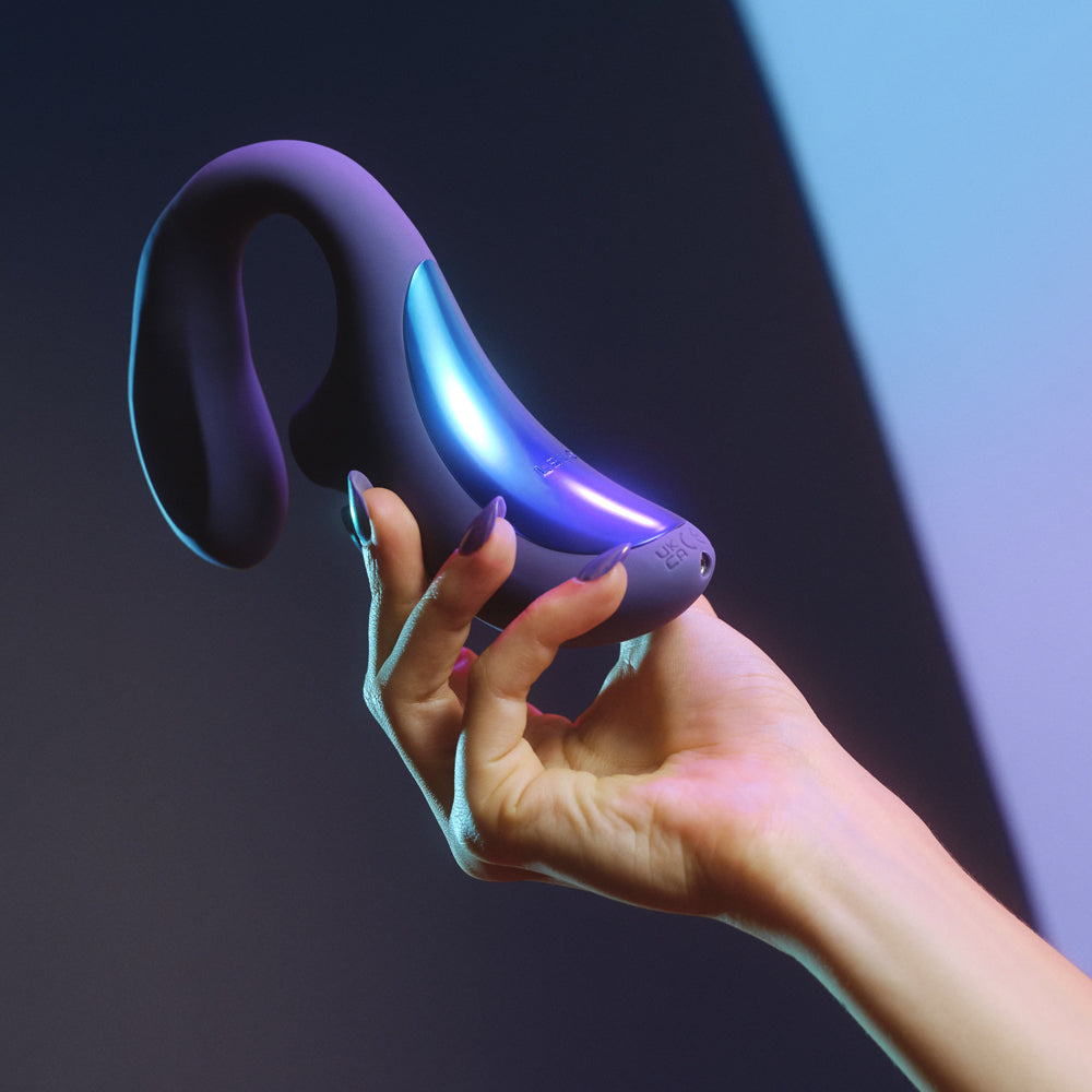 A manicured hand holds the purple silicone Lelo Enigma Wave sex toy in against a shadowy background.
