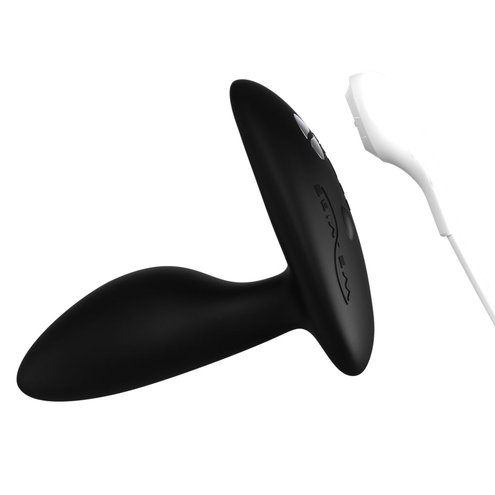 The We-Vibe Ditto+ anal plug lies on its side while its magnetic charging cable hovers over the metal connection points.
