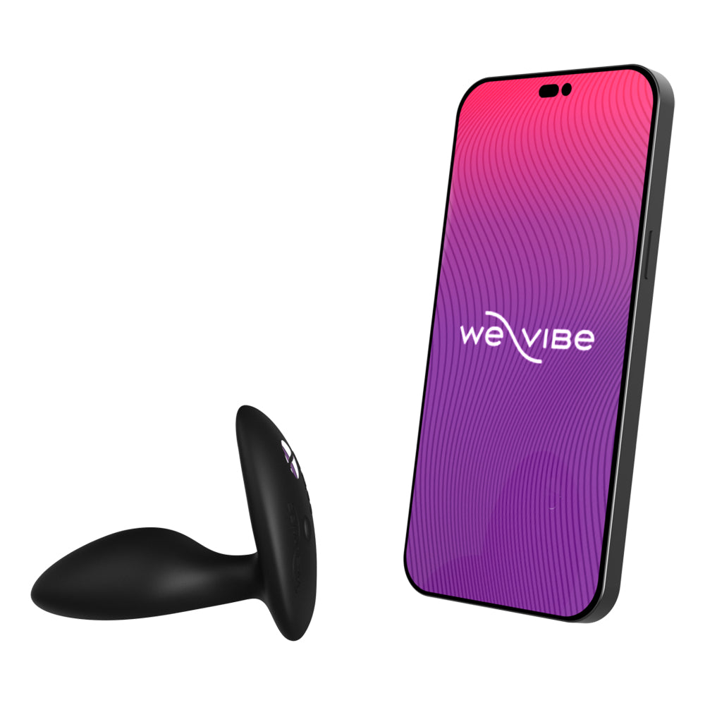 An app-compatible vibrating anal plug from We-Vibe lays next to a smartphone displaying the We-Vibe app on its screen.