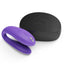 A wearable couples vibrator in purple silicone sits next to its subtle black travel case on a white background.
