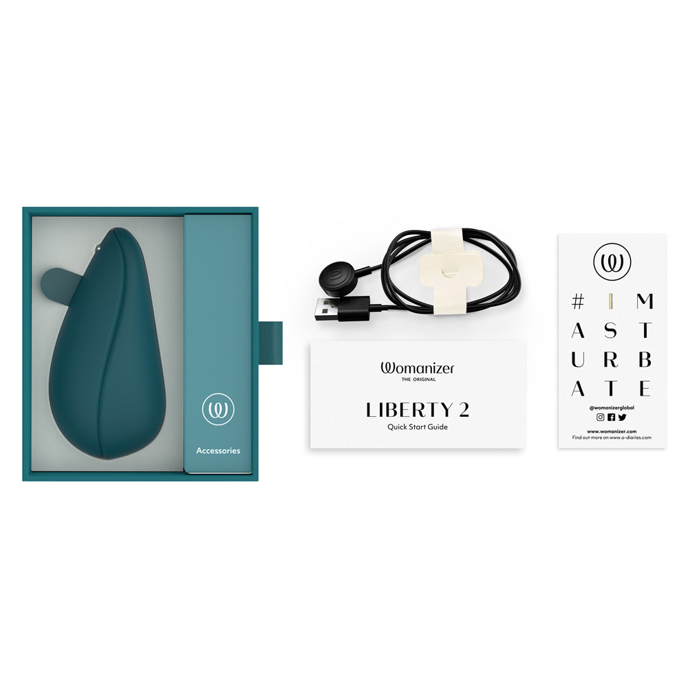 Flat lay of the Womanizer Liberty 2 Clitoral Stimulator and the included charger and instruction booklets.